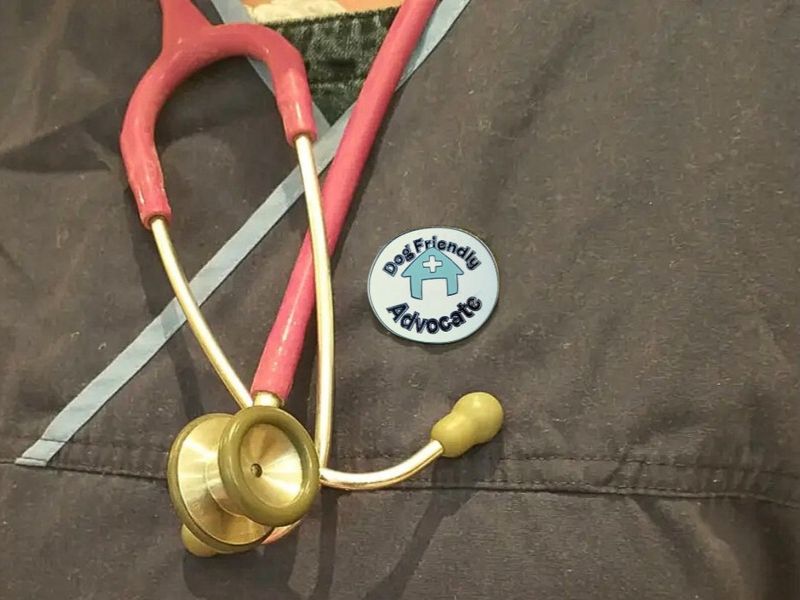 A vet wearing navy scrubs with a red stethoscope and a dog friendly advocate badge on