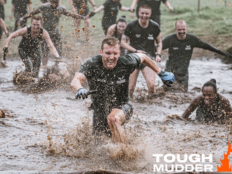 a group of people running and splashing through muddy water smiling