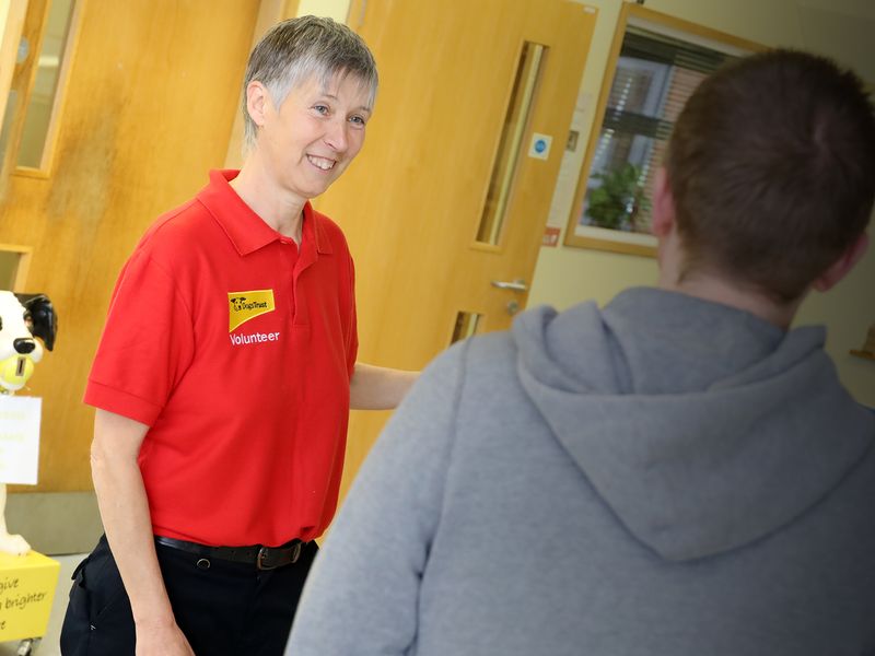 Volunteer woman wearing a red polo, greeting a man in a grey jumper