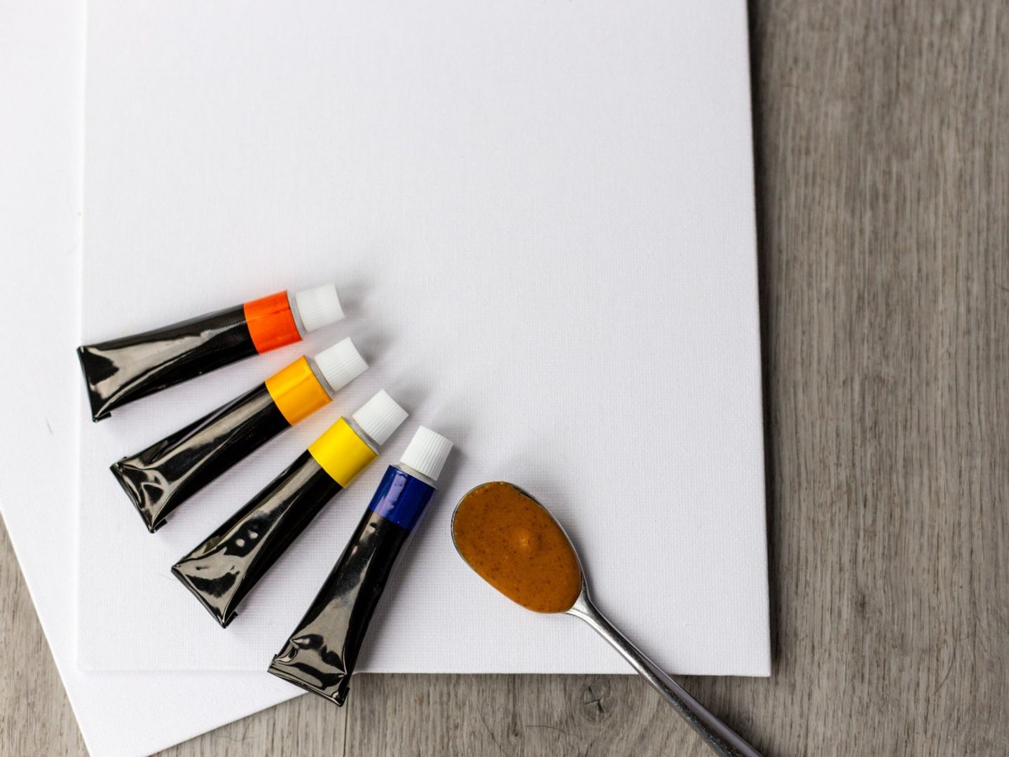 an image of a white canvas, 4 paint tubs and a teaspoon with some peanut butter on it